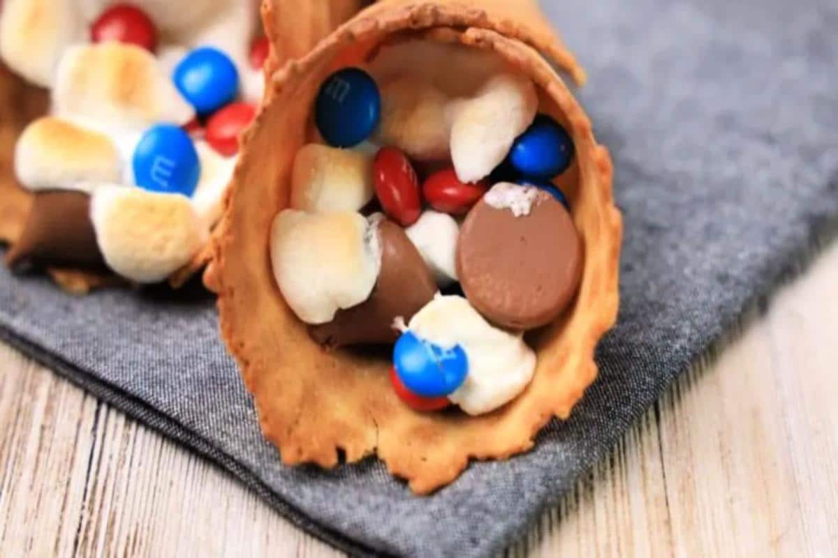 A waffle cone filled with marshmallows, chocolate candies, and chocolate pieces placed on a gray cloth sits ready to inspire fun recipes for your next gathering.