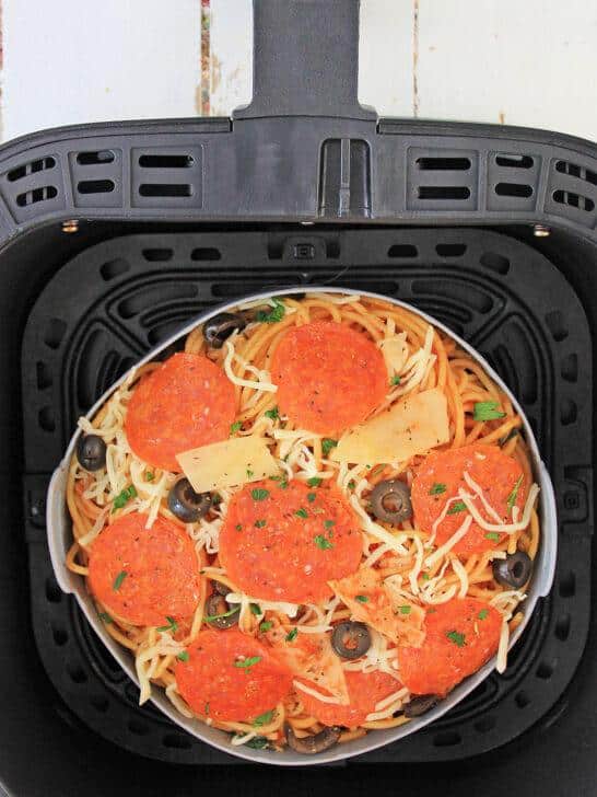 A top-down view of a black air fryer basket containing uncooked Air Fryer Loaded Pizza Pasta ready to be cooked.