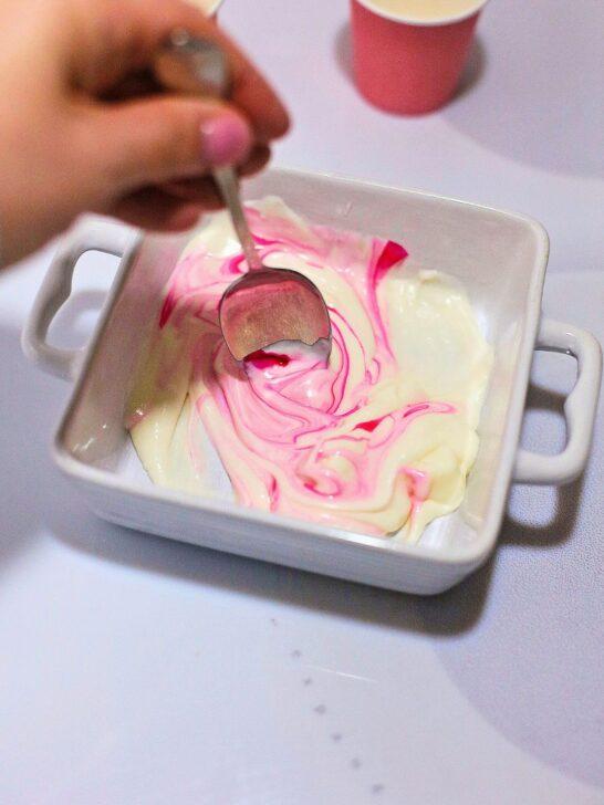 A person holding a spoon over a bowl of Bailey's Strawberry and Cream Cocoa Cups, a delightful Valentine's Day treat.