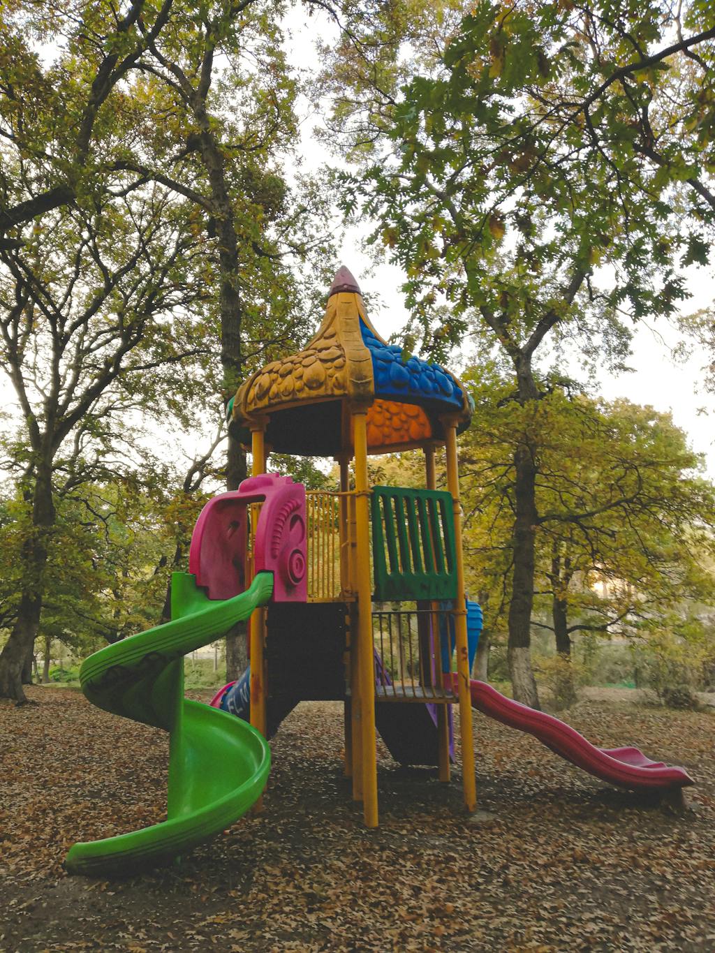 Colorful slides and structures surrounded by lush trees in an outdoor park during fall.