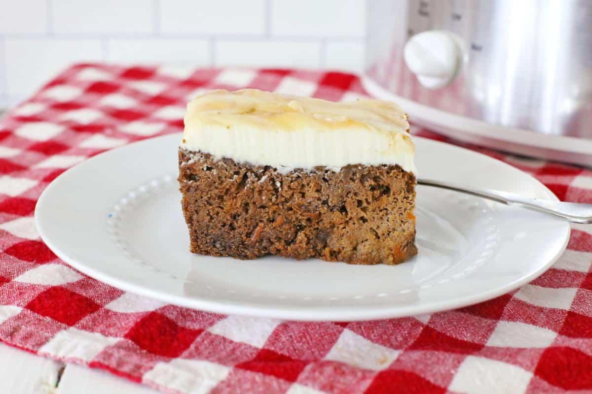 A slice of banana bread topped with cream cheese frosting, served on a white plate placed over a red and white checkered cloth, making it one of the most tempting desserts.