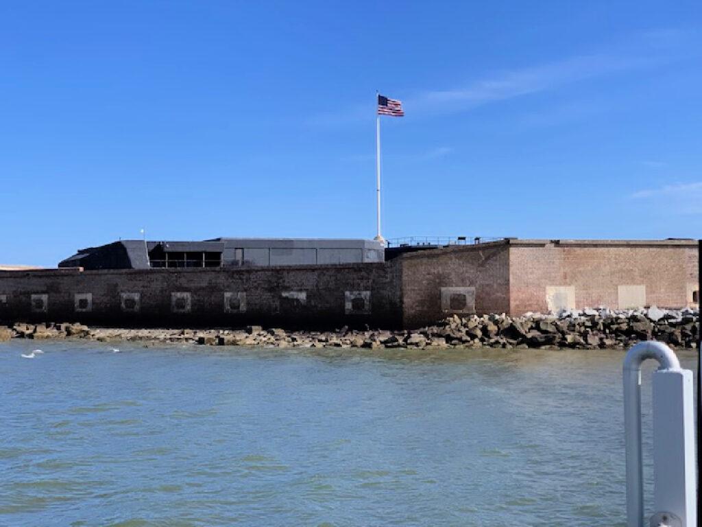 A brick fort with an American flag on a pole stands by the water under a clear blue sky—one of the many fascinating things to do in South Carolina.