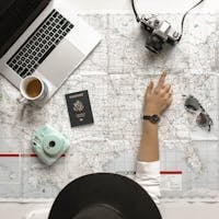 Hand on map with camera, passport, laptop, and coffee, perfect for travel planning inspiration.