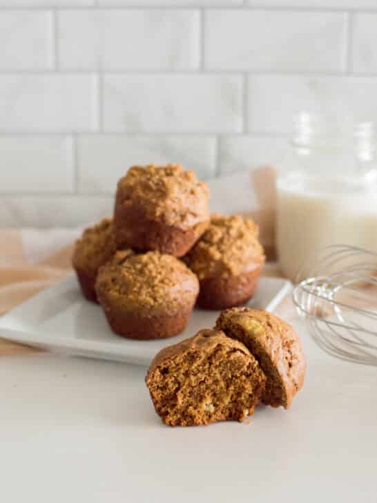 A gingerbread muffin cut in half, sitting in front of a plate of other muffins, sitting on a white plate