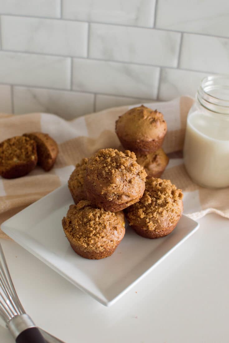 Aeriel shot of homemade gingerbread muffins on a square white plate, sitting on a wire rack with a plaid napkin and a glass of milk