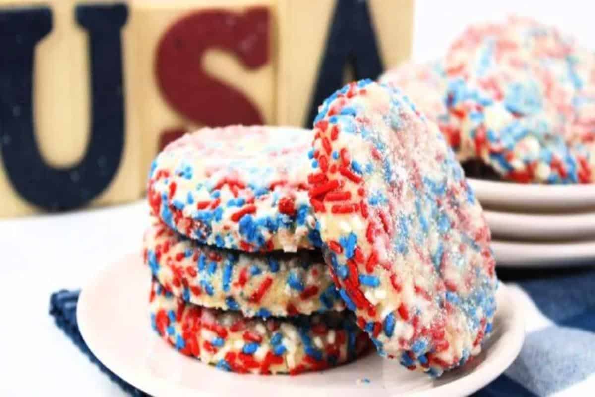 Plate of red, white, and blue sprinkle-coated sweet desserts, with a "usa" decorative sign in the background.