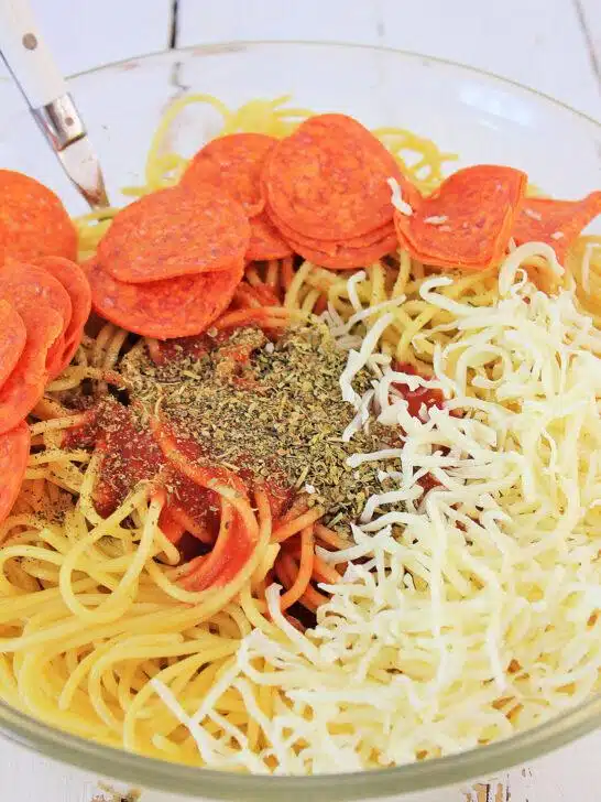 A bowl of Air Fryer Loaded Pizza Pasta topped with slices of pepperoni, shredded cheese, and a sprinkle of herbs on a wooden table.