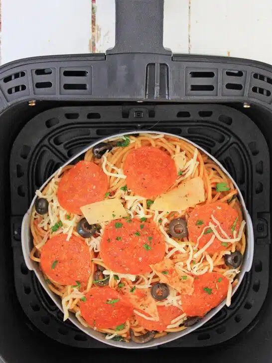 A top-down view of a black air fryer basket containing uncooked Air Fryer Loaded Pizza Pasta ready to be cooked.