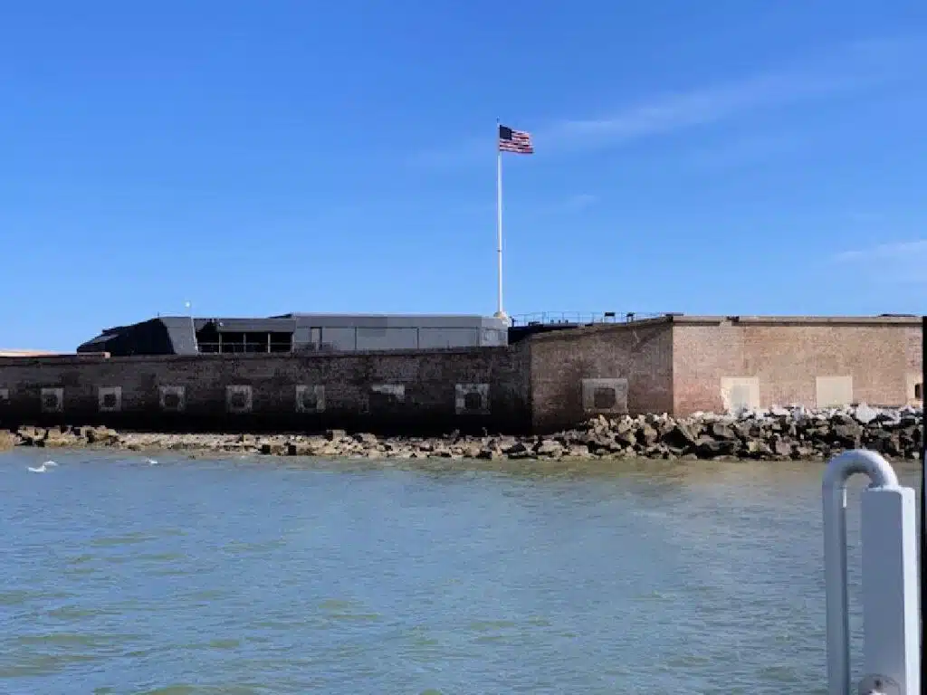 A brick fort with an American flag on a pole stands by the water under a clear blue sky—one of the many fascinating things to do in South Carolina.