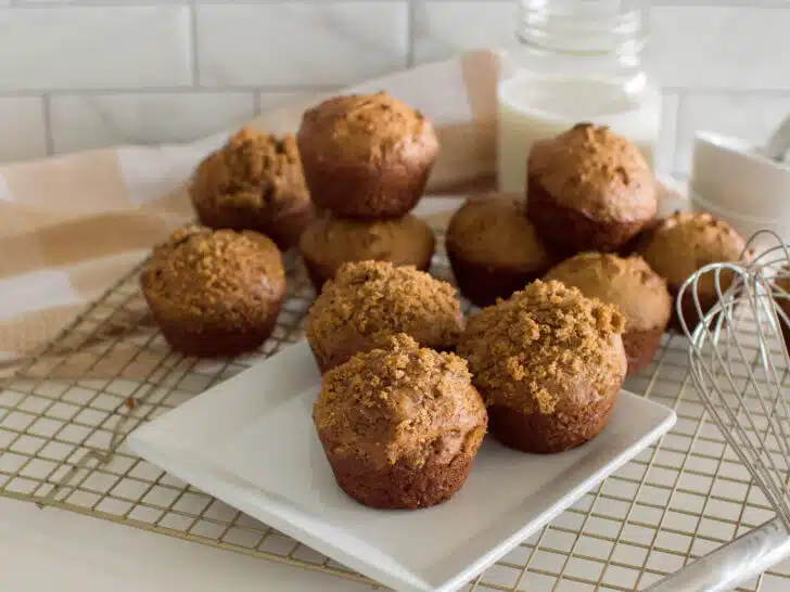 Homemade gingerbread muffins on a square white plate, sitting on a wire rack with a plaid napkin and a glass of milk