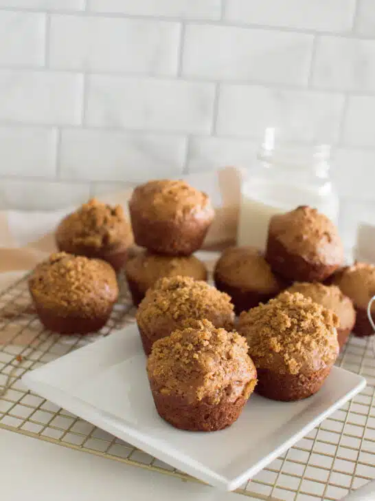 Homemade gingerbread muffins on a square white plate, sitting on a wire rack with a plaid napkin and a glass of milk