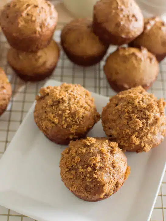 Aeriel shot of homemade gingerbread muffins on a square white plate, sitting on a wire rack with a plaid napkin and a glass of milk