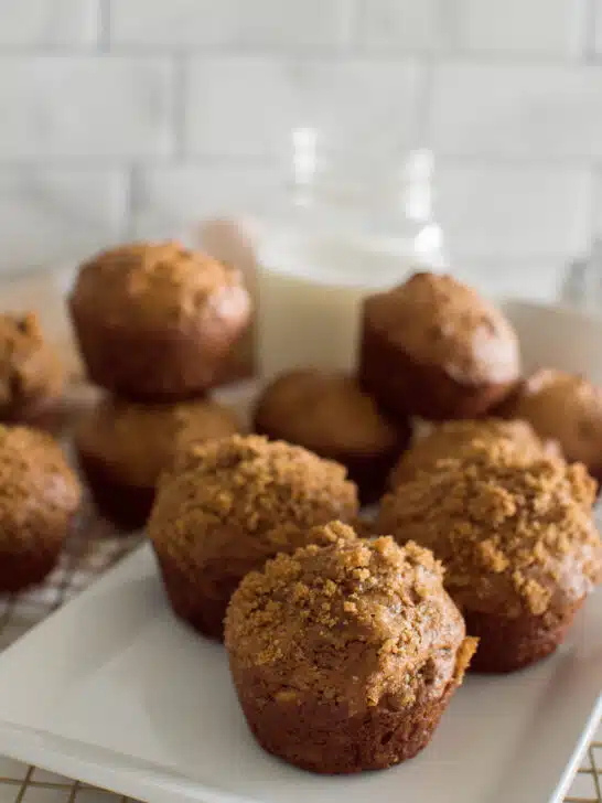 Homemade gingerbread muffins on a square white plate, sitting on a wire rack with a plaid napkin and a glass of milk