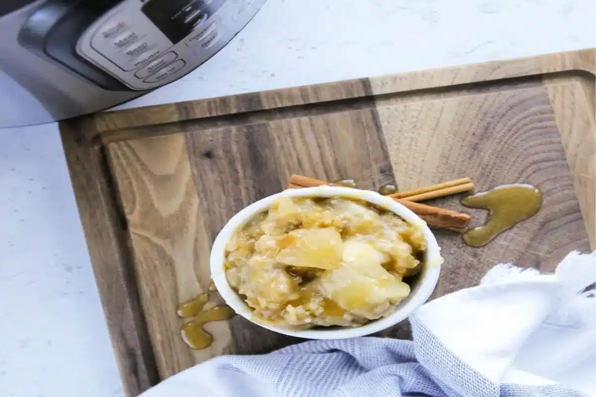 A bowl of apple sauce with cinnamon sticks on a wooden board, a napkin, and a bottle nearby, viewed from above. This tempting dessert is ready to be enjoyed.