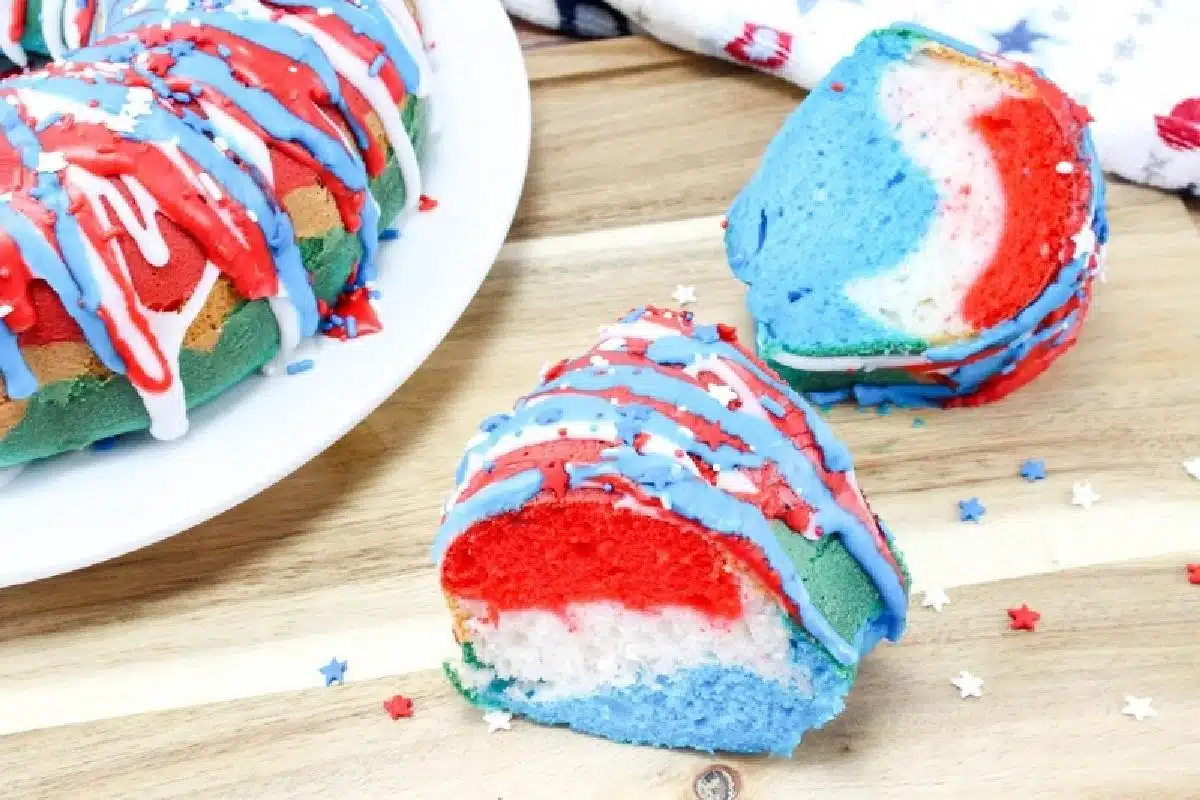 A slice of a tricolor bundt cake with red, white, and blue layers, topped with red, white, and blue icing and star-shaped sprinkles, placed on a wooden surface. Perfect for any collection of fun or patriotic recipes.